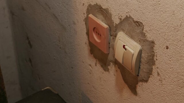 A male hand reaches for an old light switch on a rough plaster wall in a dark red room. Concept of suspense, horror atmosphere, darkness, fear, manual power, and turning off the lights.