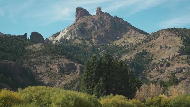 Wide shot of the prominent Cerro Montura Chilena mountain peak towering over a forested hillside in Valle Encantado, Patagonia, Argentina.