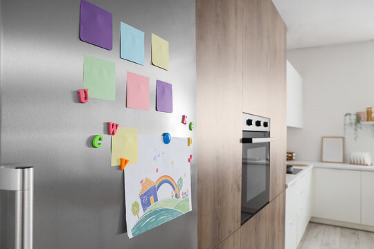Colorful sticky notes and childs drawing on stainless steel refrigerator in modern kitchen interior