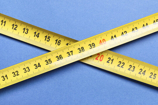 Yellow measuring tape intersecting on blue background, precision measurement and construction tools