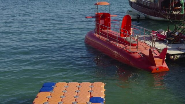 Small Red Submarine Water Vessel Moored Near Pier For Sea Excursions. Tourist Underwater Ship. Leisure Tourism