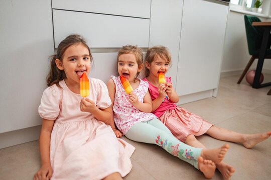 Three girls enjoy vibrant ice pops while sitting indoors