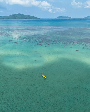 Aerial view of a yellow kayak floating on the clear turquoise waters of a shallow coral reef near the coast of Koh Samui, Chang Wat Surat Thani, Thailand.