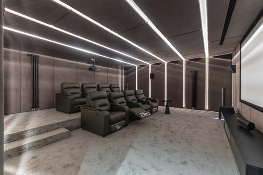 A home theater shows comfortable seating arranged for movie watching. Soft carpet covers the floor. Bright lights create a modern look. The projector is ready for films