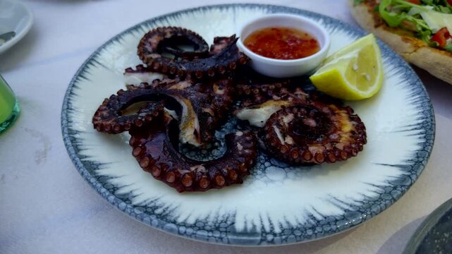 Grilled Octopus Tentacles With Fresh Lemon Slice And Sauce Bowl. Mediterranean Seafood Dish