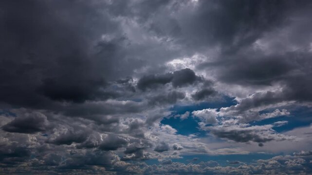 Dramatic dark storm clouds roll across a deep blue sky in an accelerated time-lapse sequence. Heavy overcast layers shift to reveal brief patches of bright blue and distant sunlight.