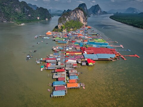 Aerial view of the floating village of Koh Panyi with colorful stilt houses and a mosque nestled against a towering limestone karst in Ko Panyi, Phang Nga, Thailand.