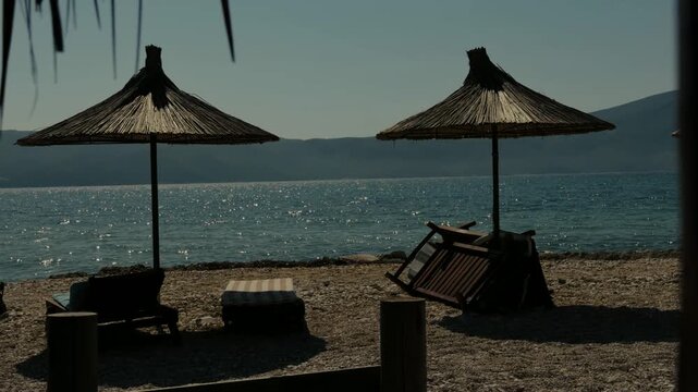 Straw Beach Umbrellas And Wooden Sun Loungers On Pebble Shore. Resort Coastline. Summer Vacation 