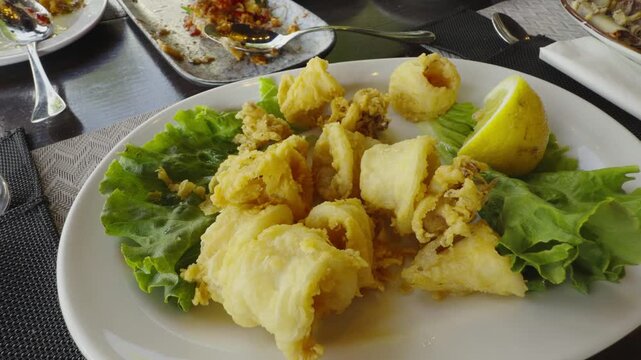Crispy Deep Fried Calamari Rings With Green Lettuce Leaves And Fresh Lemon Slice. Mediterranean Seafood Appetizer Dish