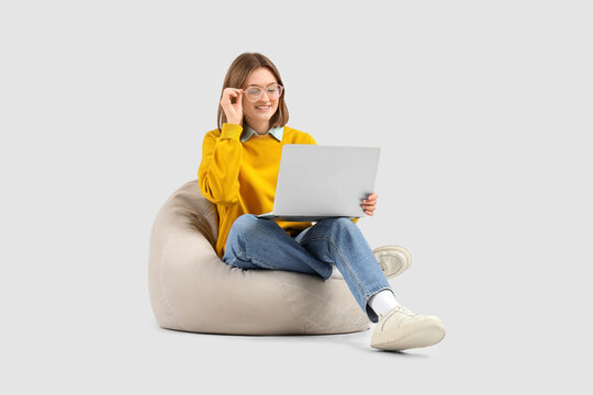 Happy female programmer with laptop sitting on beanbag chair against grey background