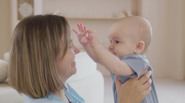 Caucasian mother hugging with Playful smiling baby enjoy lively interaction. Neutral tones and authentic lighting. Emotional motherhood comfort scene