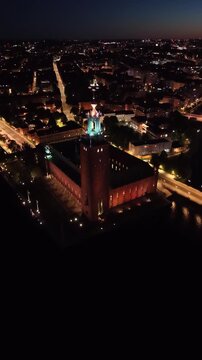 High-angle perspective of Stockholm City Hall tower illuminated at dusk. Professional night drone photography showcasing Scandinavian architecture and the M&auml;laren lake horizon.