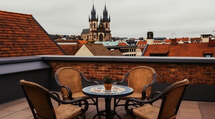 Obraz premium Rooftop terrace seating area with ornate table overlooks old city. Wicker chairs are arranged for relaxation with distant church spires under cloudy sky.