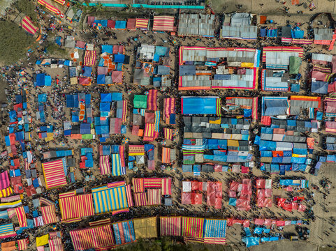 Aerial view of a vibrant outdoor market with colorful striped stalls and crowded pathways between vendors in Bogura, Rajshahi Division, Bangladesh.