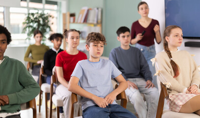 Attentive teenage students listening to lecture while female teacher stands in blurred background © JackF