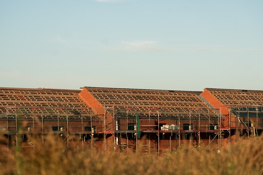 Row of Brick Houses Under Construction With Scaffolding And Roof In Progress Behind Meadow Grass, The Concept of Real Estate Development