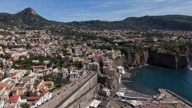 Aerial view of Meta di Sorrento colorful buildings, Marina di Alimuri beach, tuff cliffs, and lush green hills overlooking the Gulf of Naples, Italy