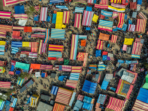 Aerial view of a bustling outdoor market filled with colorful striped tents and numerous people moving between stalls in Bogura, Rajshahi Division, Bangladesh.