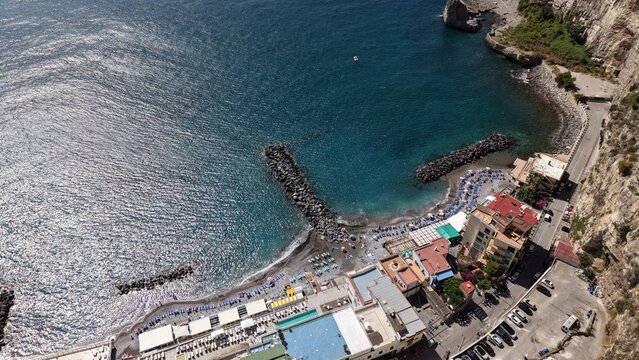 Marina di Alimuri beach with colorful umbrellas, breakwater, crystal clear turquoise water, and tuff cliffs in Meta di Sorrento, Naples, Italy