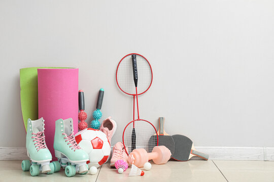 Different sports equipment, roller skates and sneakers near light wall