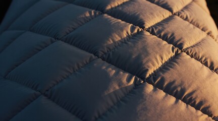 Naklejka premium Closeup of quilted puffer material showing texture and light play. Soft, padded fabric with diamond pattern stitch detail. Warm, modern textile surface.