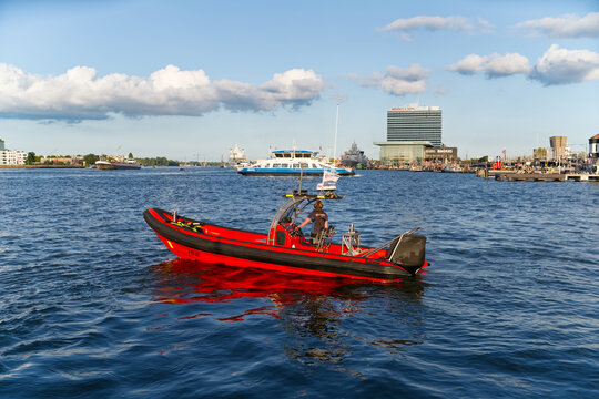 Amsterdam, Netherlands - August 24, 2025: A bright red RIB boat cruising and surveilling on the IJ river in Amsterdam during Sail Amsterdam event on sunny day with the city skyline