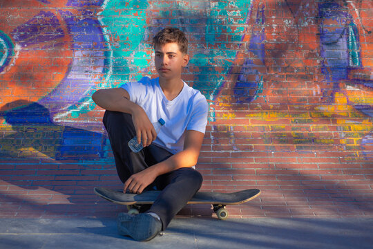 Boy sitting on a skateboard with a bottle in his hand
