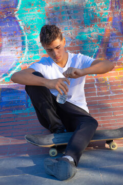 Young skateboarder resting with a bottle of water next to a colorful urban mural