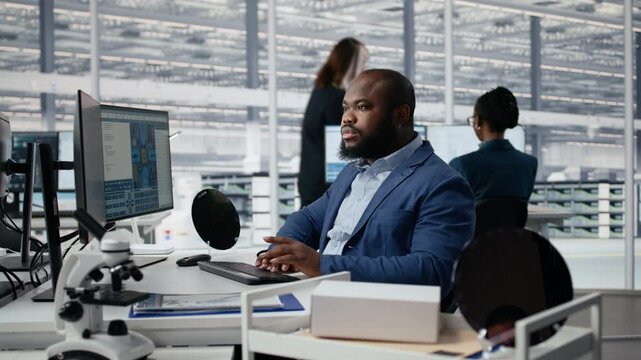 Man examining microchip circuit layouts on monitor in factory R&D office using specialized software, improving manufacturing, semiconductor used in smart devices and African American worker.