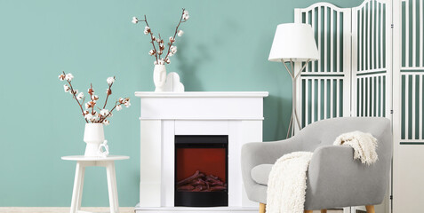 Obraz premium Interior of stylish living room with grey armchair, fireplace and cotton flowers
