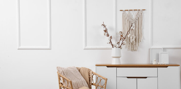 Interior of light living room with armchair, commode and cotton flowers in vase