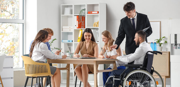 Young man in wheelchair using laptop with human resources commission during job interview at office
