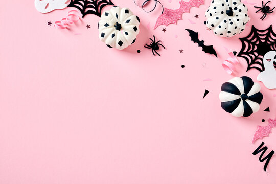 Creative pastel Halloween flat lay. Black and white striped and polka dot pumpkins, bats, and spiderwebs on a pink background with left-aligned copy space.