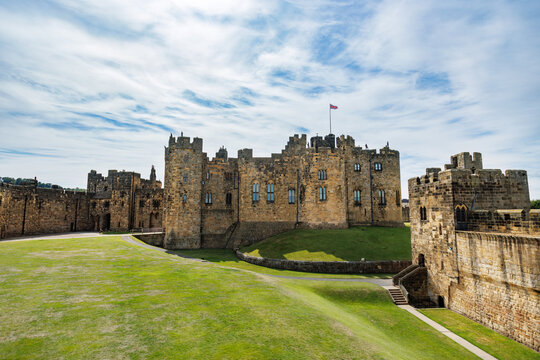 Historic medieval Alnwick castle on grassy lawn under blue sky