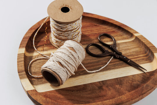 Close up of cotton twine spool with decorative string and vintage scissors on wooden tray, rustic diy craft supplies and handmade packaging materials
