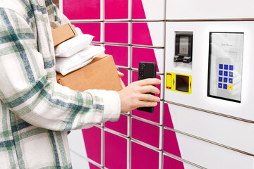 Person holding packages and using a smartphone at an automated parcel locker terminal. Convenient contactless pickup and delivery service for online ecommerce shopping logistics. © Kyrylo