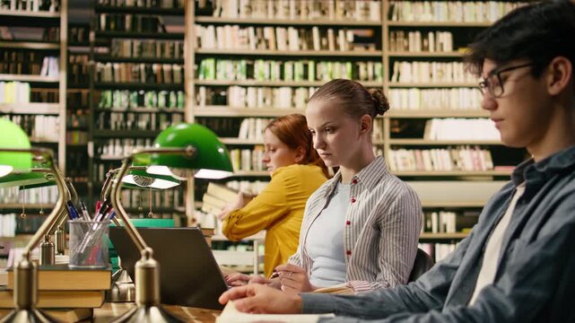 Student discussing assignment with tutor at university library desk, surrounded by books, green lamps and study materials for coursework, Focused study group for guidance and mentoring.