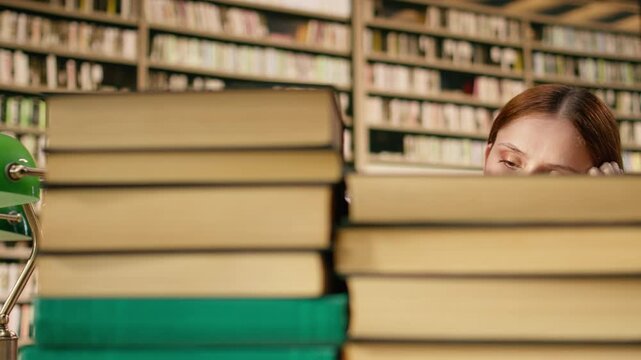 Overwhelmed young woman holding her head near tall stack of books at library table, emphasizing study materials overload and intense exam preparation, Finals pressure study session.