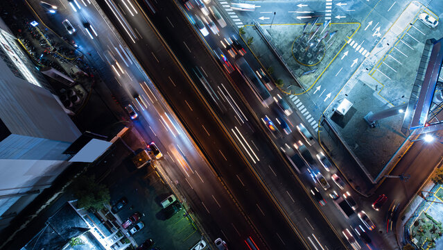 Aerial view of a busy highway at night with long exposure light trails from moving vehicles, illuminated road markings, and surrounding urban infrastructure in the Dominican Republic.
