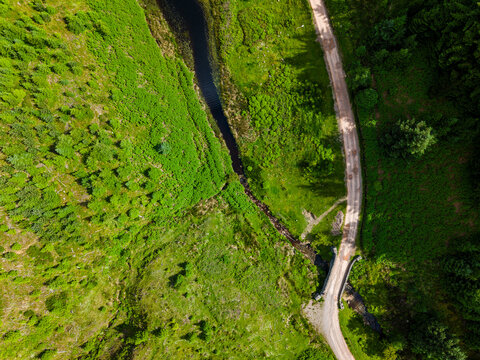 Looking down at a winding dirt road and stone bridge over a stream in Wales