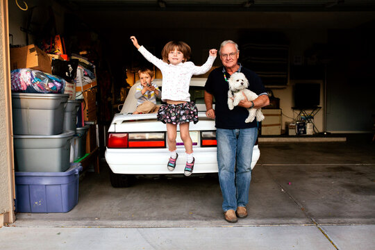 Girl jumping off car; with grandpa, brother and dog