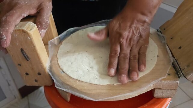 Woman using a wooden tortilla press making corn tortillas