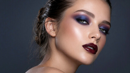 Fototapeta premium Black Cherry Lip Gloss Metallic Midnight Blue Gel Eyeshadow and Cream Highlighter Skincare Makeup Products on Beauty Model With Feminine Aesthetic and Charcoal Blue Copy Space Banner