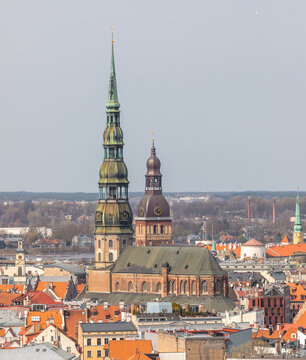Aerial view of the historic spires of St. Peter's Church and Riga Cathedral rising above the orange rooftops of the old town in Riga, Latvia.