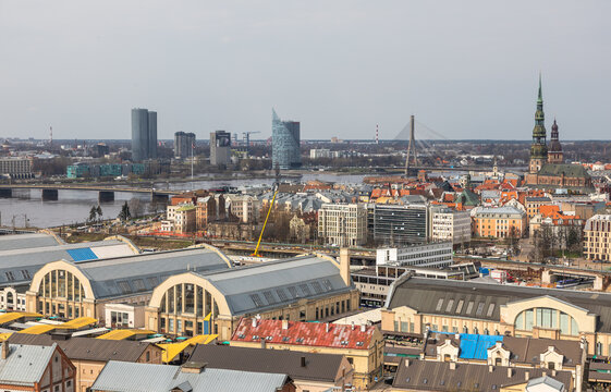 Aerial view of Riga Central Market with its distinctive arched pavilions, the Daugava River, and the historic skyline featuring St. Peter's Church in Riga, Latvia.