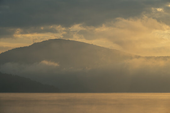 Misty mountain silhouette over a calm lake at golden hour, Żywiec Lake