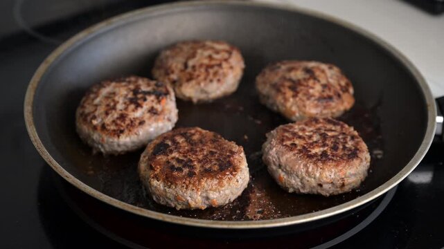 Beef and turkey patties frying in black pan with browned crust. Cooking video with sizzle sound