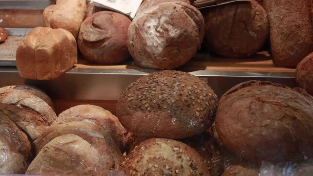A close up view of fresh baked bread loaves at a bakery or market, with a variety of textures and toppings, slow dynamic motion