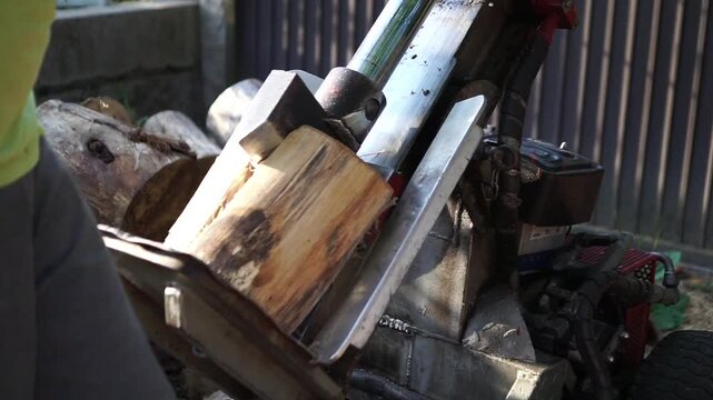 Side view of a man operating a hydraulic log splitter, carefully adjusting a thick piece of wood to cut it into smaller, manageable firewood logs