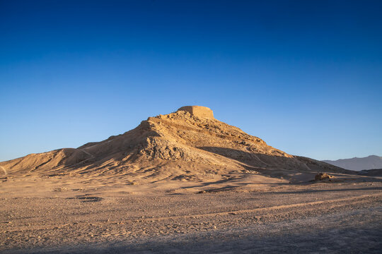 Morning light over the Towers of Silence hill near Yazd, Iran, set in an empty desert landscape. The Dakhma site represents Zoroastrian burial tradition and Iran's ancient religious heritage.